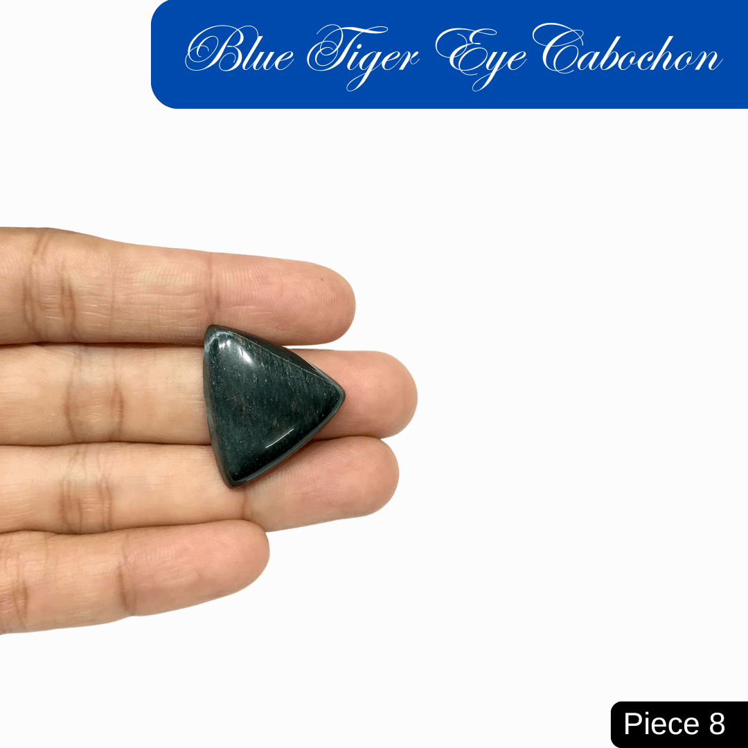 Hand holding a triangular blue tiger eye cabochon with a deep blue sheen and chatoyant bands. Piece 8.