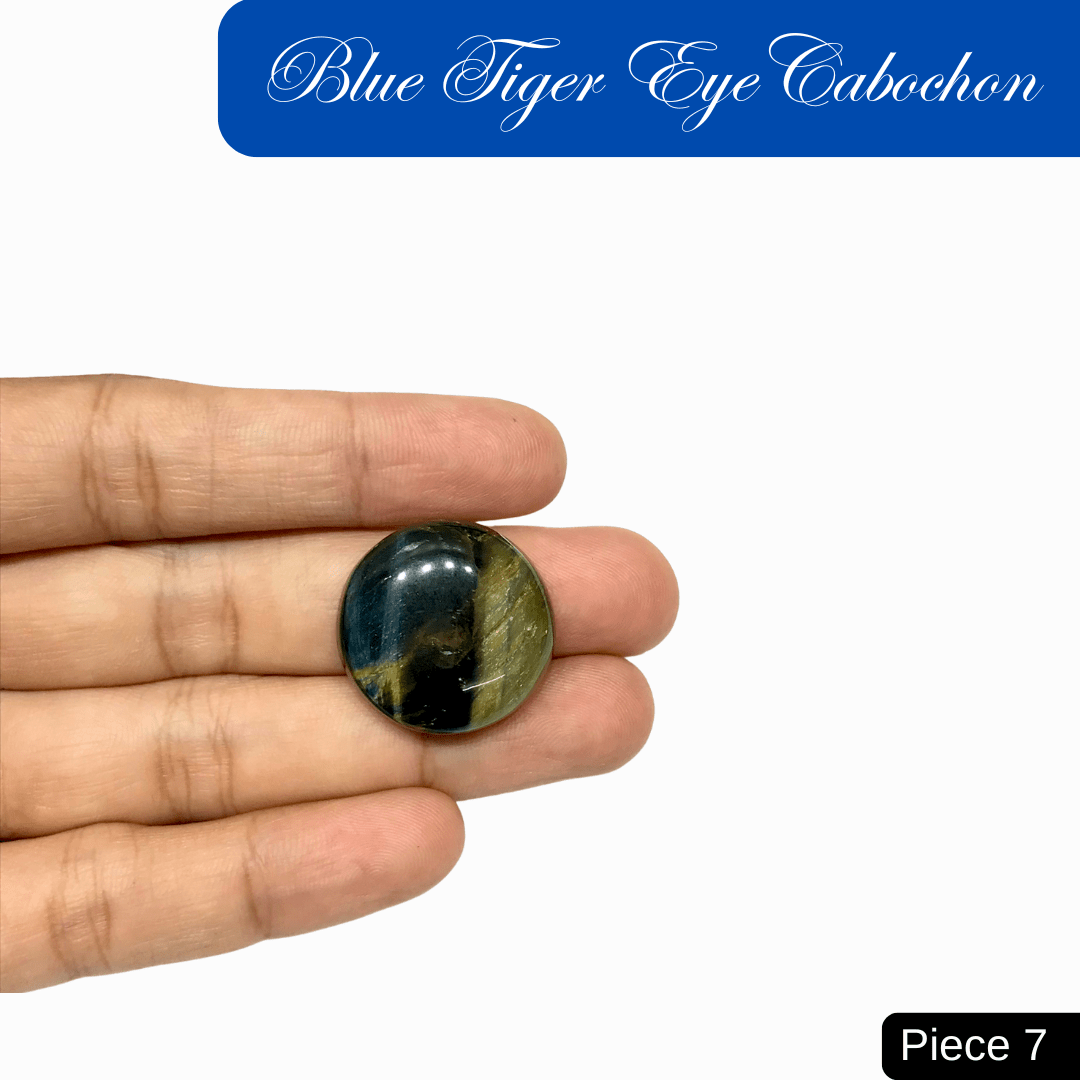 Hand holding a Blue Tiger Eye Cabochon with silky luster and deep blue sheen, showcasing chatoyant bands and cool, calming energy.