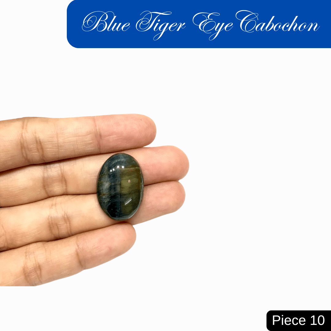 Hand holding blue tiger eye cabochon with deep blue sheen and chatoyant bands, known for calm confidence and protection. Piece 10.