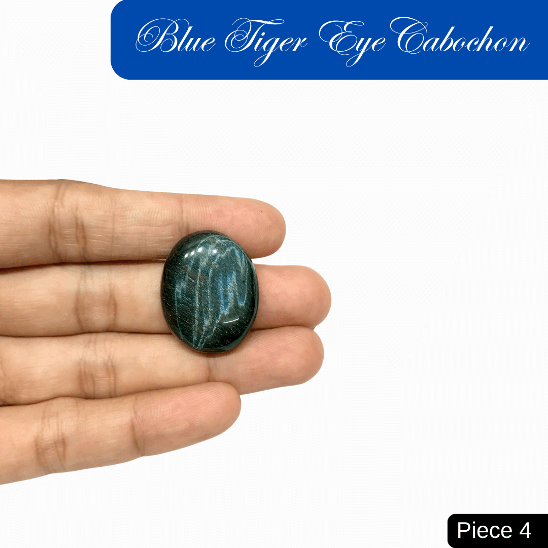 Blue Tiger Eye Cabochon with deep blue sheen, known for calming energy, held between fingers, showcases silky luster and chatoyant bands.