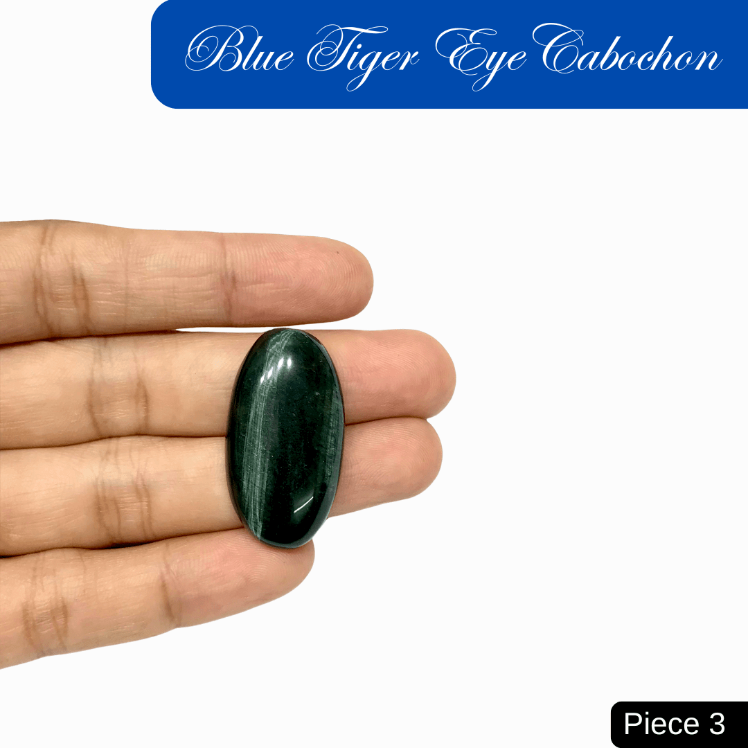 Hand holding a blue tiger eye cabochon with deep blue sheen and chatoyant bands, symbolizing calm, protection, and clarity.