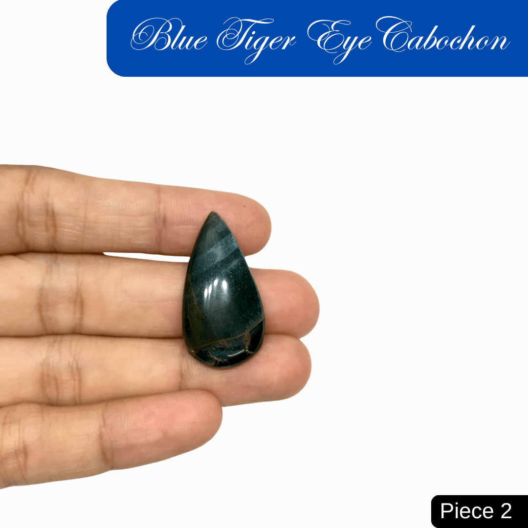 Hand holding a teardrop blue tiger eye cabochon with silky luster and chatoyant bands, symbolizing calm and protection.