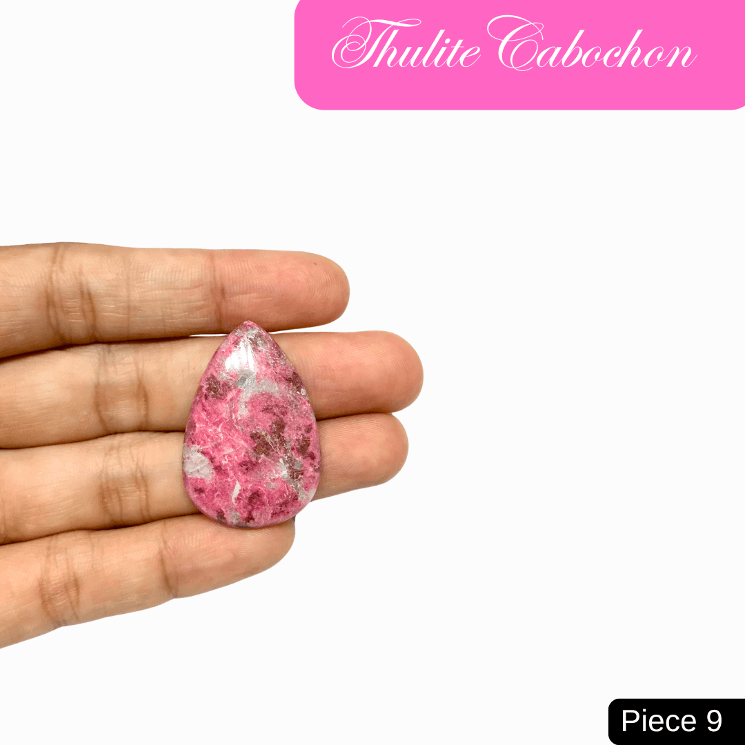 Hand holding a teardrop-shaped Thulite cabochon with vibrant pink shades, known for love and emotional healing properties.