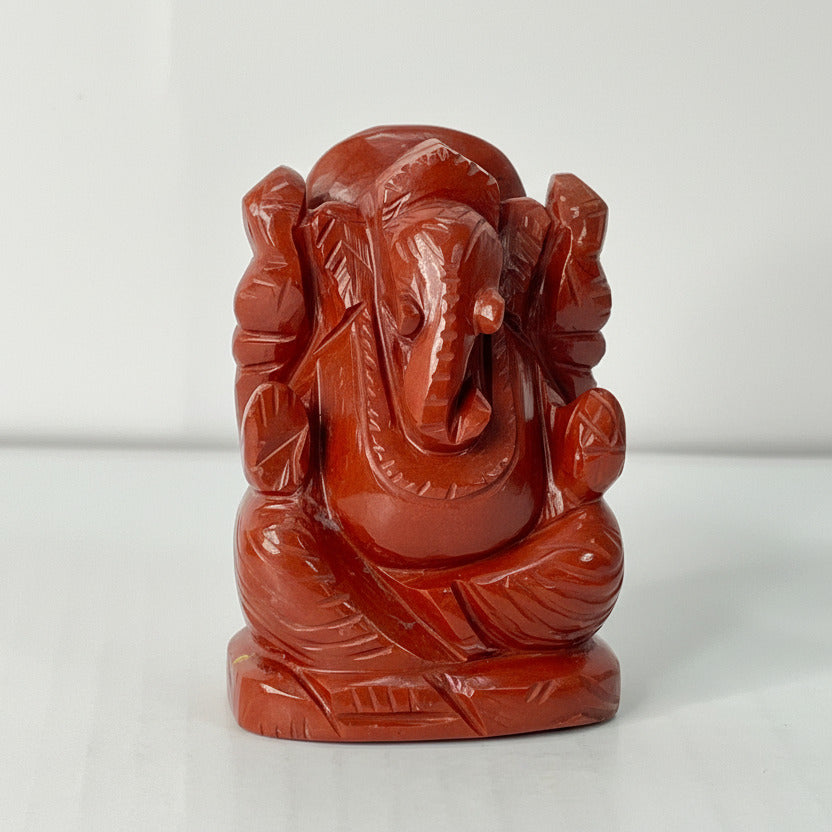 Red stone statue of a seated figure with multiple arms on a white background