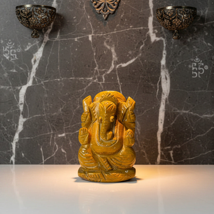 Brown stone statue of a seated figure with elephant head on a white background