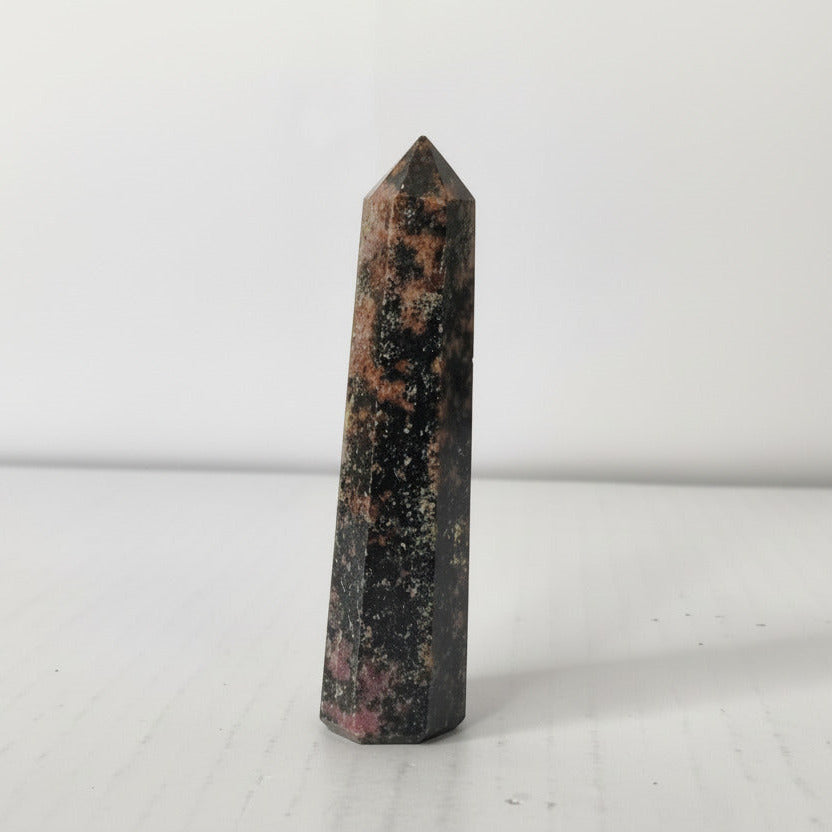 Tall, dark-colored crystal obelisk on a light gray background