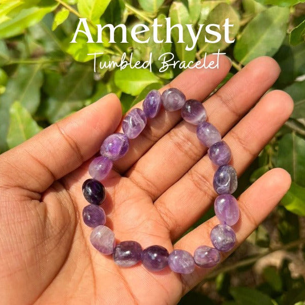 Amethyst tumbled bracelet held in a hand with green leaves in the background