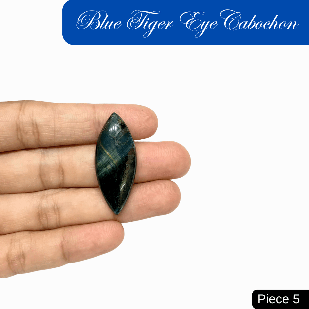 Hand holding a blue tiger eye cabochon with silky luster and chatoyant bands, symbolizing insight, calm confidence, and protection.