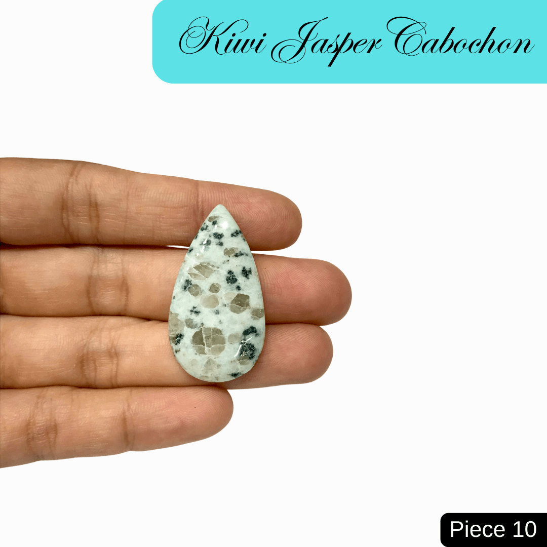 Hand holding teardrop Kiwi Jasper cabochon, soft green with black and cream speckles, promotes tranquility and emotional balance.