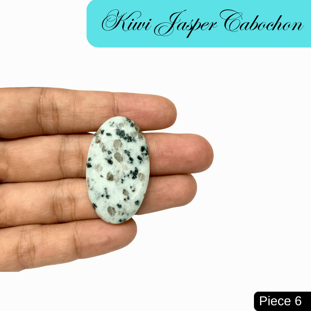 Hand holding an oval Kiwi Jasper cabochon with soft green hues speckled with black, promoting tranquility and emotional strength.