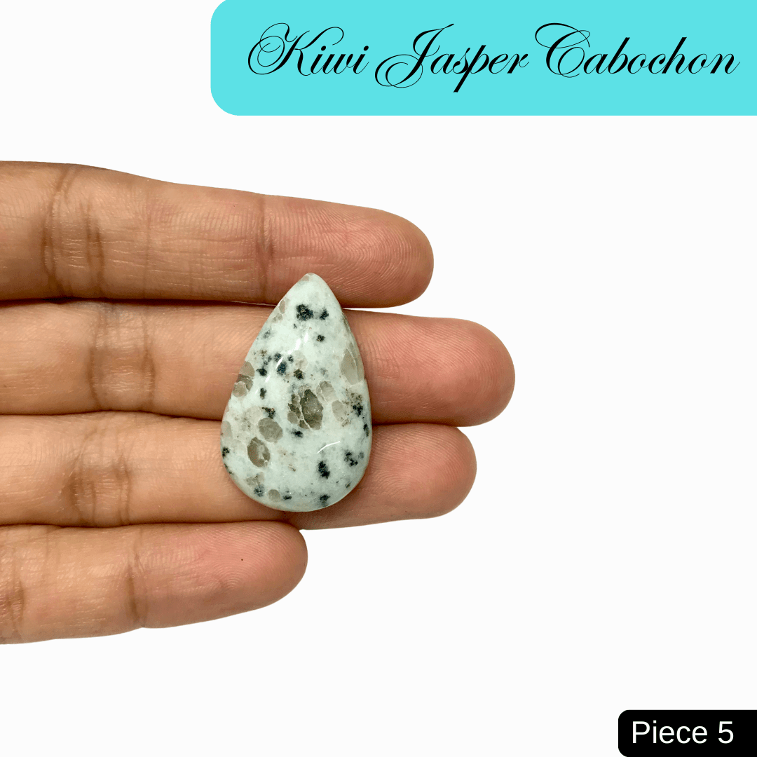 Hand holding a pear-shaped Kiwi Jasper cabochon, showcasing its soft green hue with black and cream speckles, known for nurturing energy.