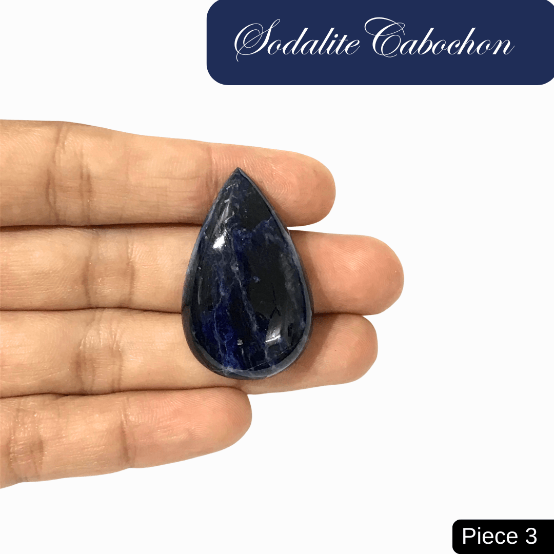 Hand holding a teardrop-shaped sodalite cabochon featuring rich blue tones and white calcite veins, known for mental clarity and intuition.