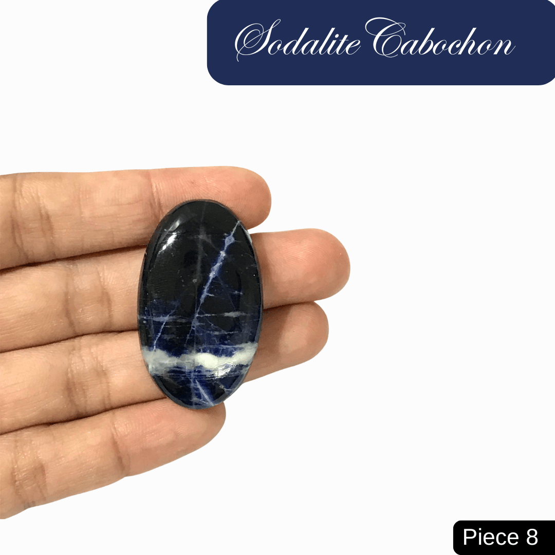 Hand holding an oval sodalite cabochon with rich blue tones and white calcite veins, known for enhancing intuition and communication.