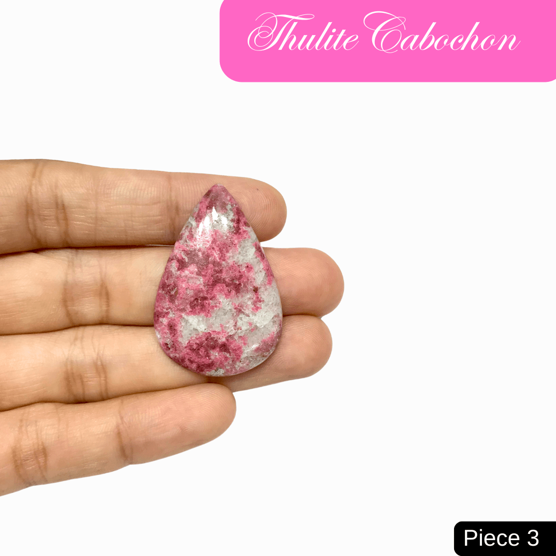 Hand holding a teardrop-shaped Thulite cabochon, showcasing vibrant pink colors ideal for love and emotional healing.